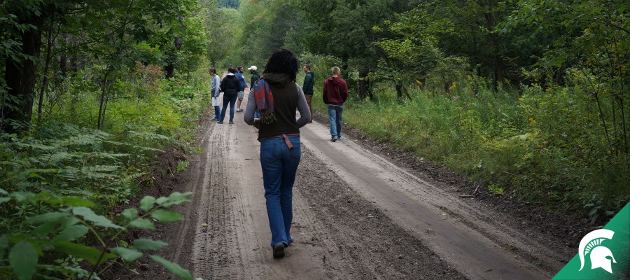 Students walking along a gravel road in a wooded area